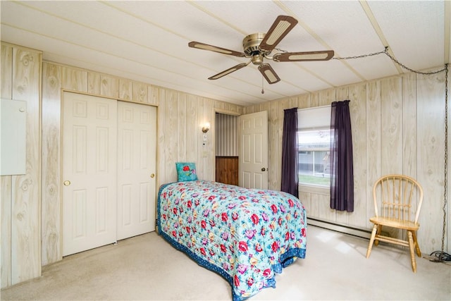 carpeted bedroom with ceiling fan, baseboard heating, a closet, and wood walls