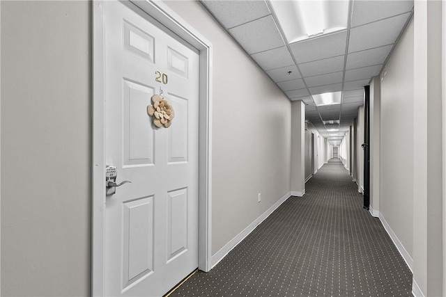 hallway featuring dark carpet, baseboards, and a drop ceiling