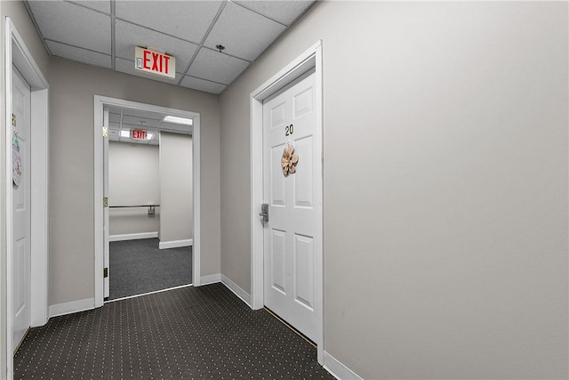 hall featuring dark carpet, baseboards, and a drop ceiling