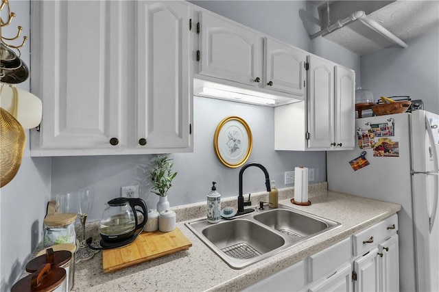 kitchen featuring a sink, light countertops, freestanding refrigerator, and white cabinetry