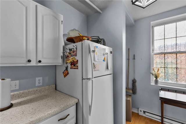 kitchen with light stone countertops, light wood-type flooring, a baseboard radiator, freestanding refrigerator, and white cabinetry