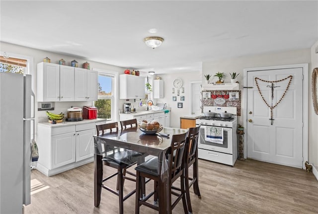 kitchen featuring freestanding refrigerator, white range with gas cooktop, a sink, and light wood-style floors