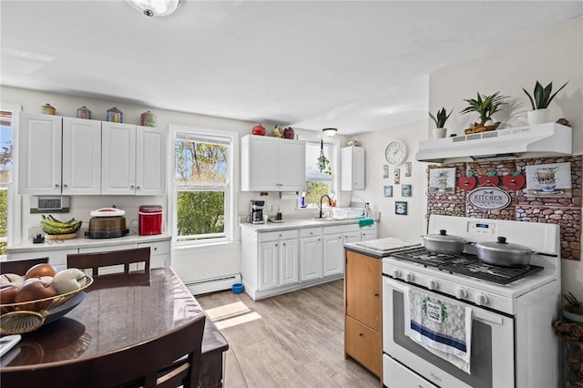 kitchen with a sink, light countertops, a baseboard radiator, under cabinet range hood, and white range with gas stovetop