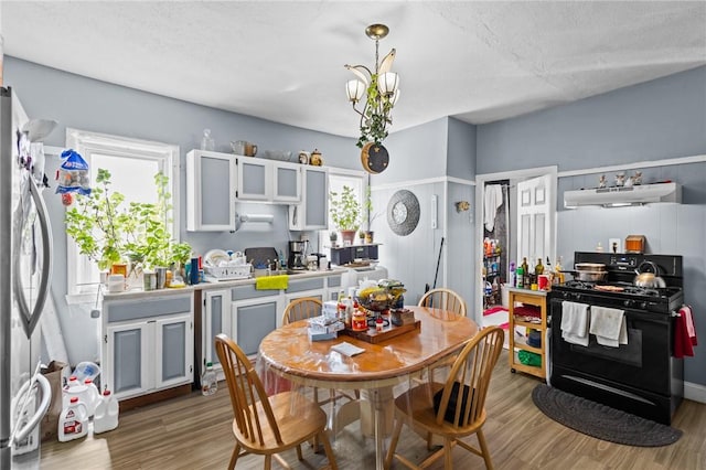 kitchen featuring ventilation hood, light wood finished floors, a textured ceiling, freestanding refrigerator, and black range with gas cooktop