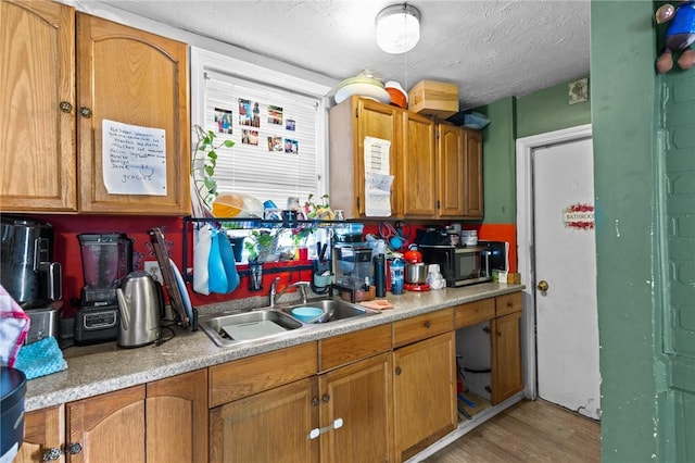 kitchen featuring brown cabinets, light wood-type flooring, a sink, light countertops, and stainless steel microwave