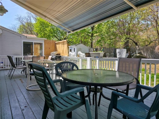 deck with a storage unit, fence, an outbuilding, and outdoor dining space