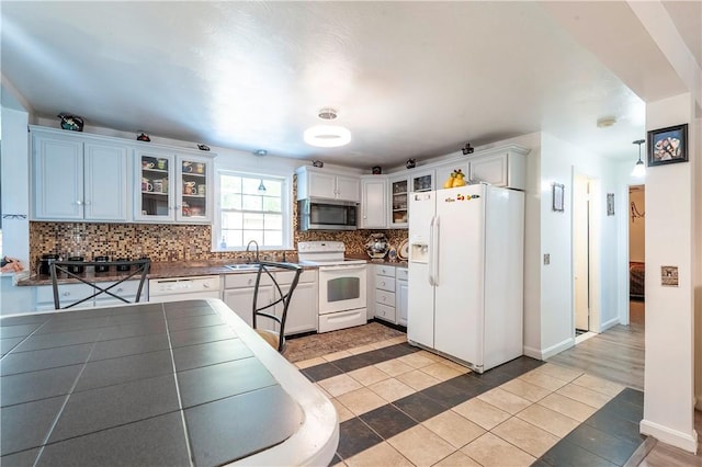 kitchen with light tile patterned flooring, dark countertops, white appliances, decorative backsplash, and glass insert cabinets