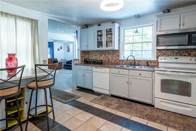 kitchen featuring white appliances, glass insert cabinets, decorative backsplash, and a sink