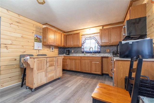 kitchen with a sink, backsplash, wood finished floors, and wood walls