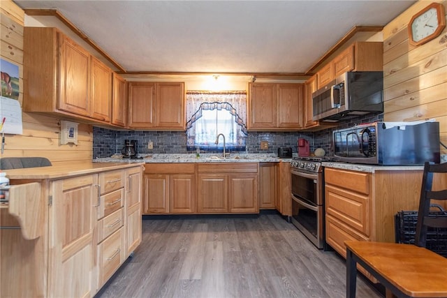 kitchen with crown molding, wood finished floors, tasteful backsplash, a sink, and appliances with stainless steel finishes