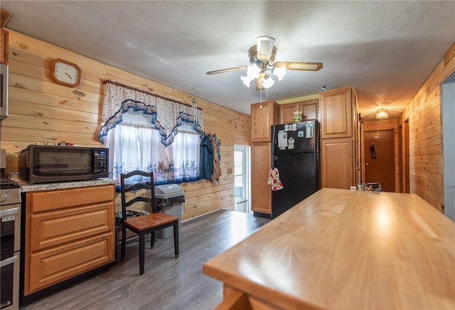 kitchen featuring dark wood-style flooring, ceiling fan, wood counters, wood walls, and black appliances