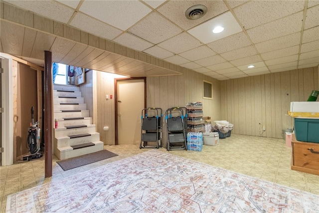 finished below grade area with wooden walls, tile patterned floors, a paneled ceiling, stairs, and visible vents