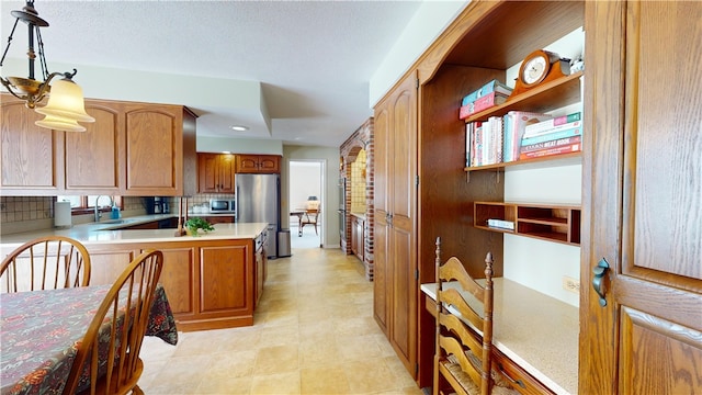 kitchen featuring backsplash, appliances with stainless steel finishes, a sink, light countertops, and a peninsula
