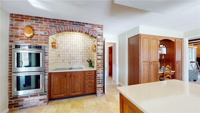 kitchen featuring brown cabinetry, stainless steel double oven, black electric stovetop, and light countertops