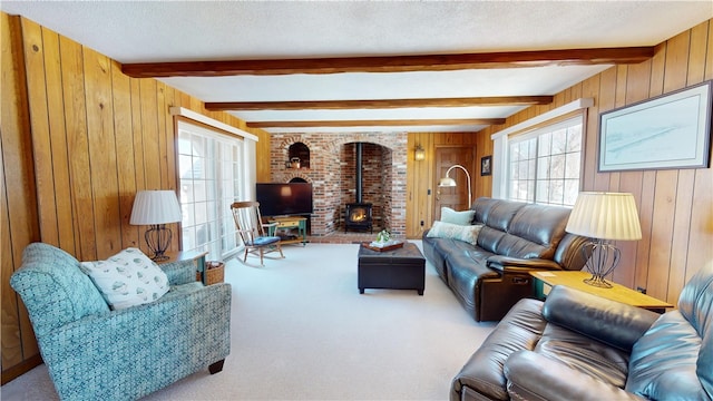 carpeted living room with wooden walls, a textured ceiling, beam ceiling, and a wood stove