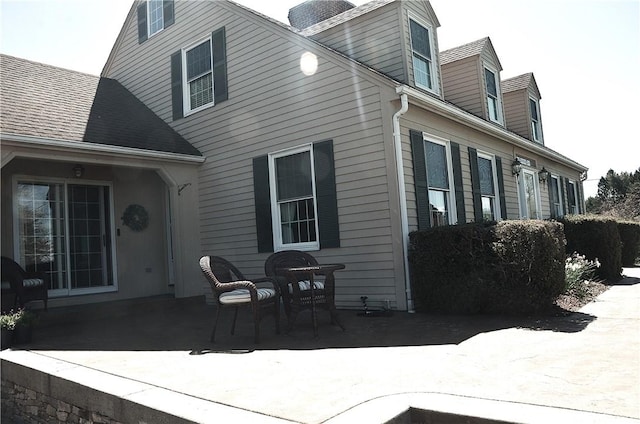 rear view of house with roof with shingles, a chimney, and a patio area
