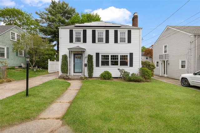 colonial inspired home with a chimney, roof mounted solar panels, and a front lawn