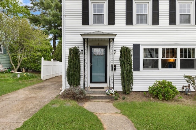 view of exterior entry with a lawn and fence