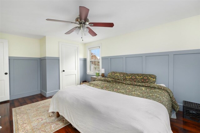 bedroom featuring wood finished floors, ceiling fan, a wainscoted wall, and a decorative wall