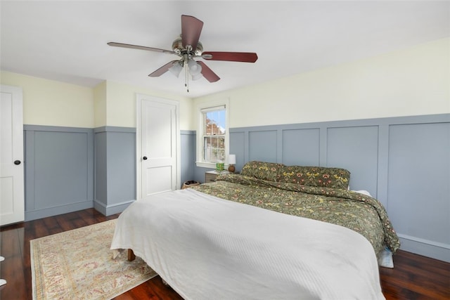 bedroom with a ceiling fan, wainscoting, wood finished floors, and a decorative wall