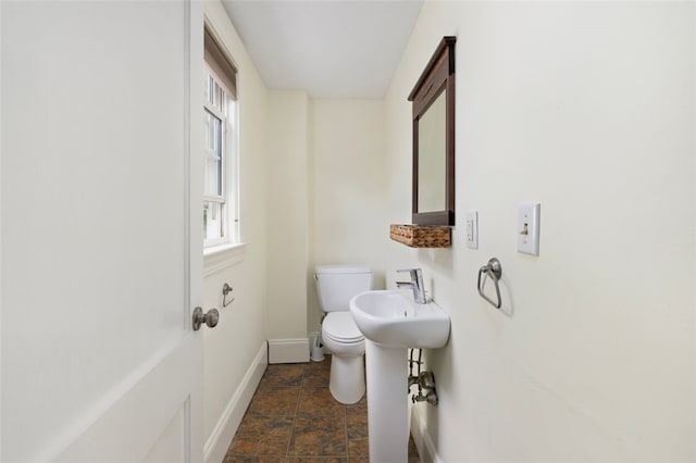 half bath with baseboards, stone finish flooring, plenty of natural light, and toilet