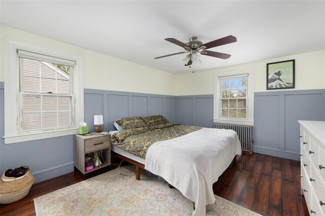 bedroom featuring a wainscoted wall, dark wood finished floors, radiator heating unit, and a decorative wall