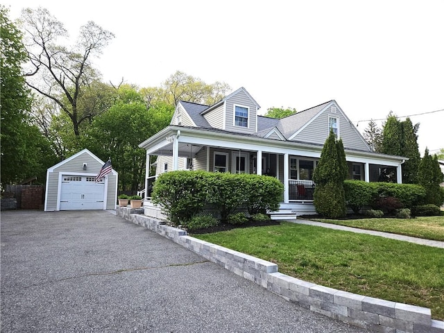 view of front facade with covered porch, a front yard, an outbuilding, a garage, and aphalt driveway
