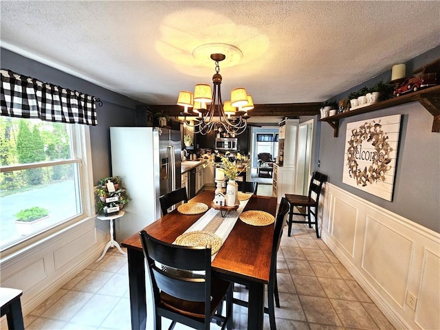dining room with a textured ceiling, a notable chandelier, a wainscoted wall, and a decorative wall