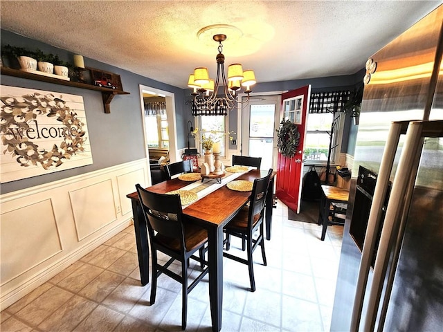 dining space with a wainscoted wall, a notable chandelier, a healthy amount of sunlight, and a decorative wall