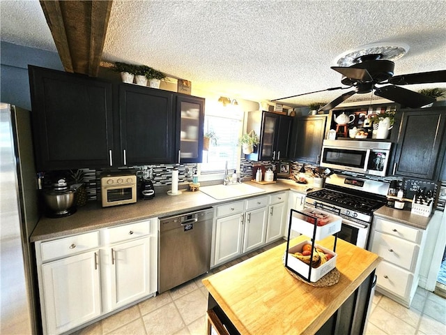 kitchen with appliances with stainless steel finishes, a sink, a textured ceiling, a ceiling fan, and white cabinetry
