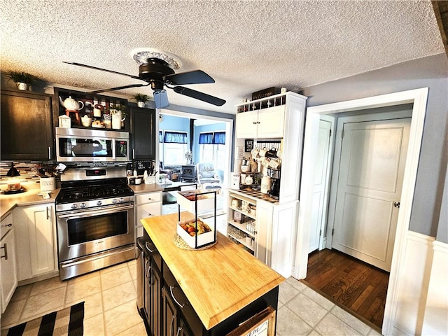 kitchen with light tile patterned flooring, ceiling fan, a textured ceiling, butcher block countertops, and stainless steel appliances