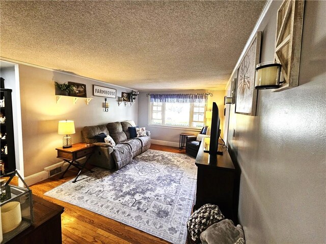 living area with baseboards, a textured ceiling, ornamental molding, and wood finished floors