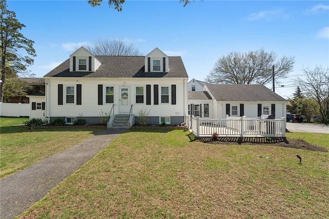new england style home with a wooden deck, roof with shingles, and a front lawn