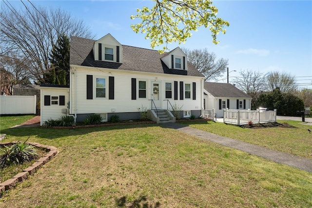 cape cod-style house with roof with shingles, fence, a wooden deck, and a front yard