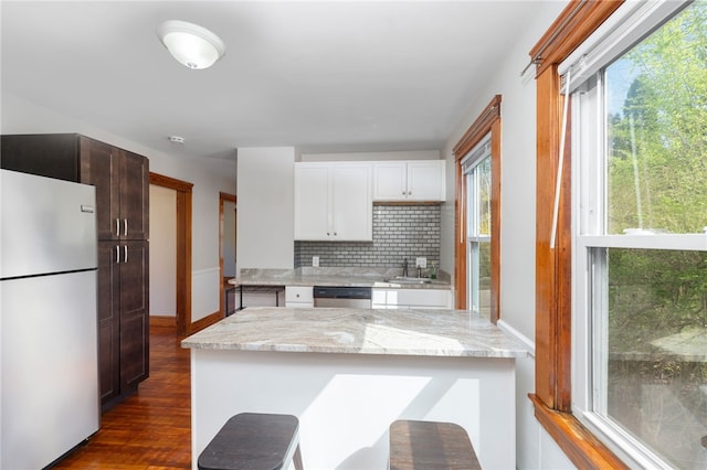 kitchen with a healthy amount of sunlight, stainless steel dishwasher, freestanding refrigerator, and backsplash
