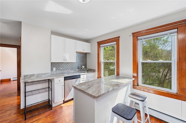 kitchen with stainless steel dishwasher, wood finished floors, baseboard heating, tasteful backsplash, and a sink