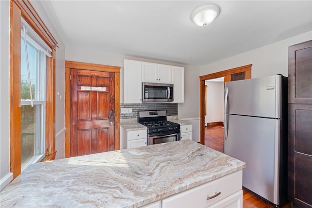 kitchen featuring wood finished floors, light stone countertops, white cabinetry, appliances with stainless steel finishes, and backsplash