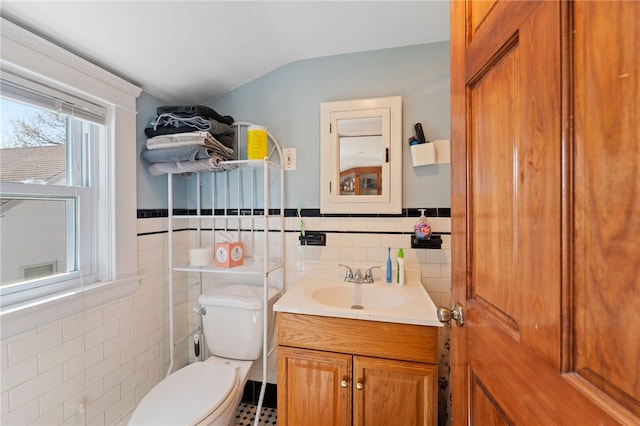 bathroom featuring tile patterned flooring, vanity, toilet, tile walls, and lofted ceiling