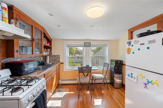 kitchen with a sink, white appliances, decorative backsplash, light wood-type flooring, and glass insert cabinets