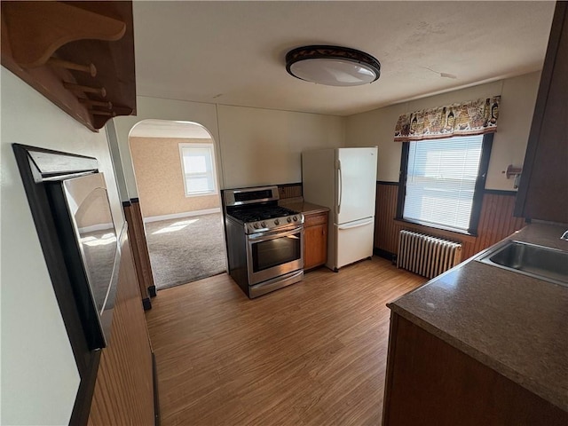 kitchen with stainless steel gas range, a sink, arched walkways, radiator heating unit, and freestanding refrigerator