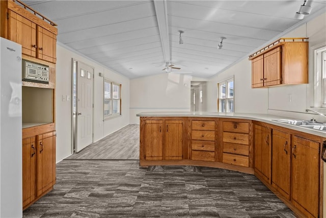kitchen featuring a ceiling fan, rail lighting, a sink, a peninsula, and vaulted ceiling with beams