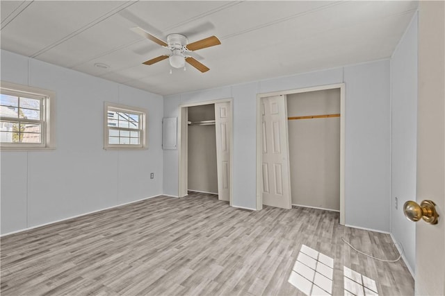 unfurnished bedroom with a ceiling fan, multiple closets, and wood finished floors