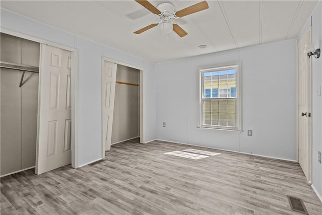 unfurnished bedroom featuring ceiling fan, multiple closets, light wood-style flooring, baseboards, and visible vents