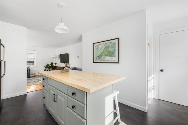 kitchen featuring hanging light fixtures, a center island, baseboards, a kitchen bar, and butcher block counters