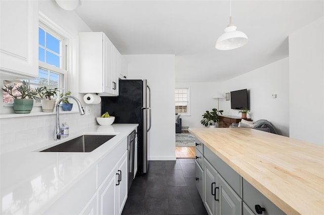 kitchen featuring wooden counters, tasteful backsplash, dishwasher, a sink, and white cabinetry