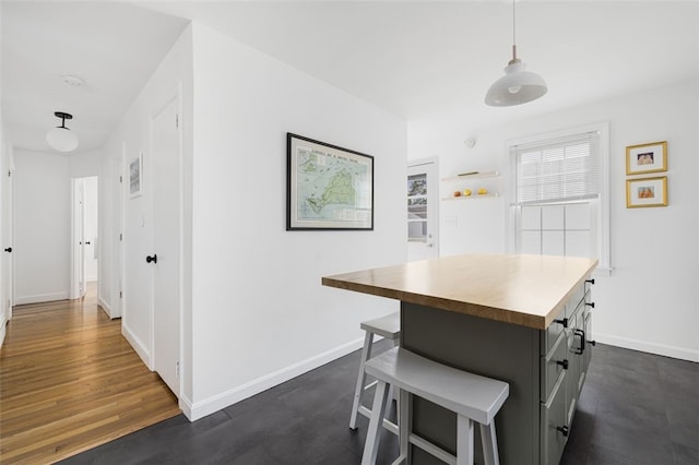 kitchen with butcher block counters, a kitchen island, baseboards, a kitchen bar, and dark wood-type flooring