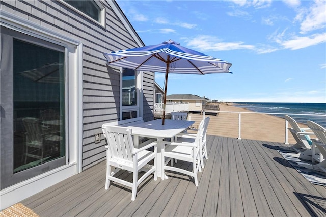 wooden deck with a beach view, a water view, and outdoor dining area