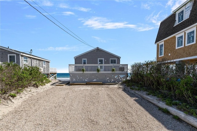 view of front of house with a shingled roof, a deck with water view, and gravel driveway
