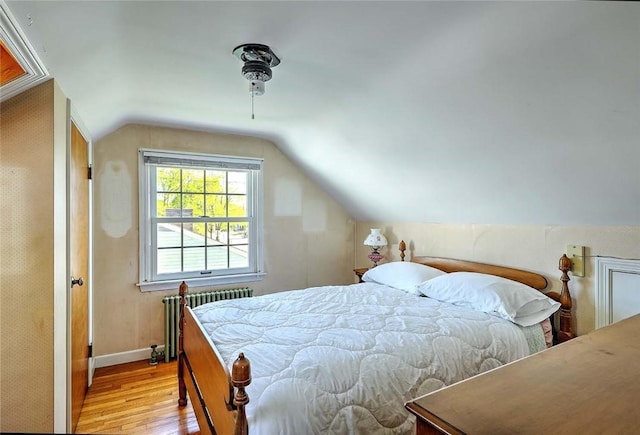 bedroom featuring baseboards, radiator heating unit, lofted ceiling, and wood finished floors