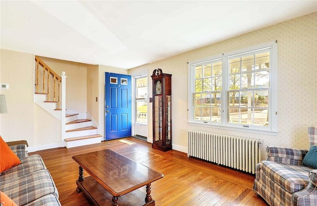 living area featuring wood finished floors, radiator heating unit, stairway, and wallpapered walls